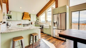A modern kitchen with green cabinets, a stainless steel refrigerator, and a large window overlooking a scenic view. - Pristine Cabin w/ Stables in Black Hawk by Casinos (Black Hawk)