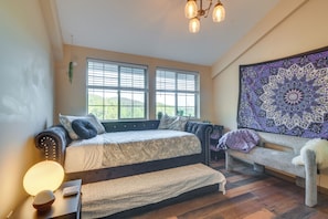 A bedroom with a bed, a bench, a tapestry, and a window with blinds.