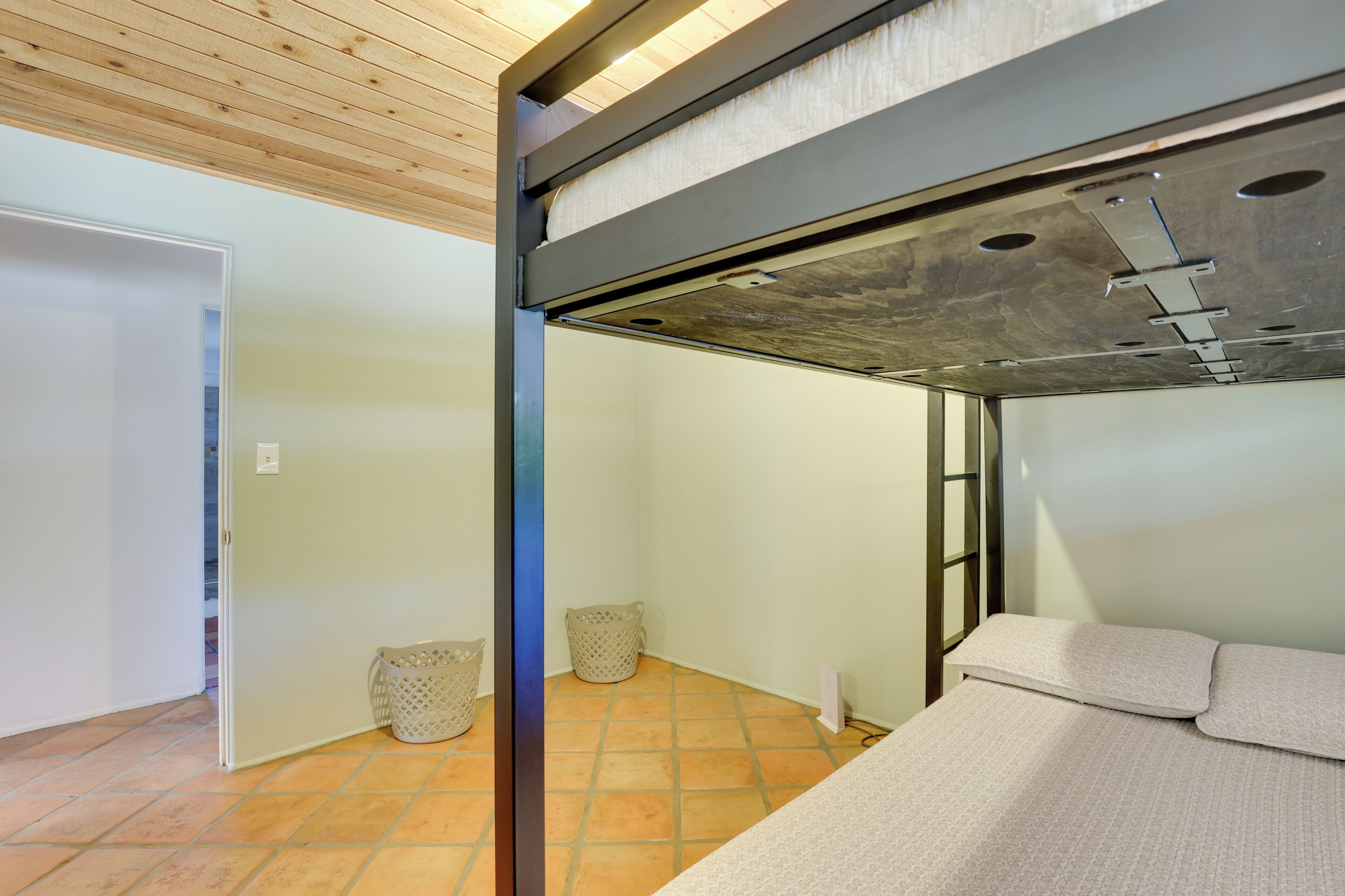 A room with a bunk bed, a wooden ceiling, a tiled floor, and a door leading to another room.