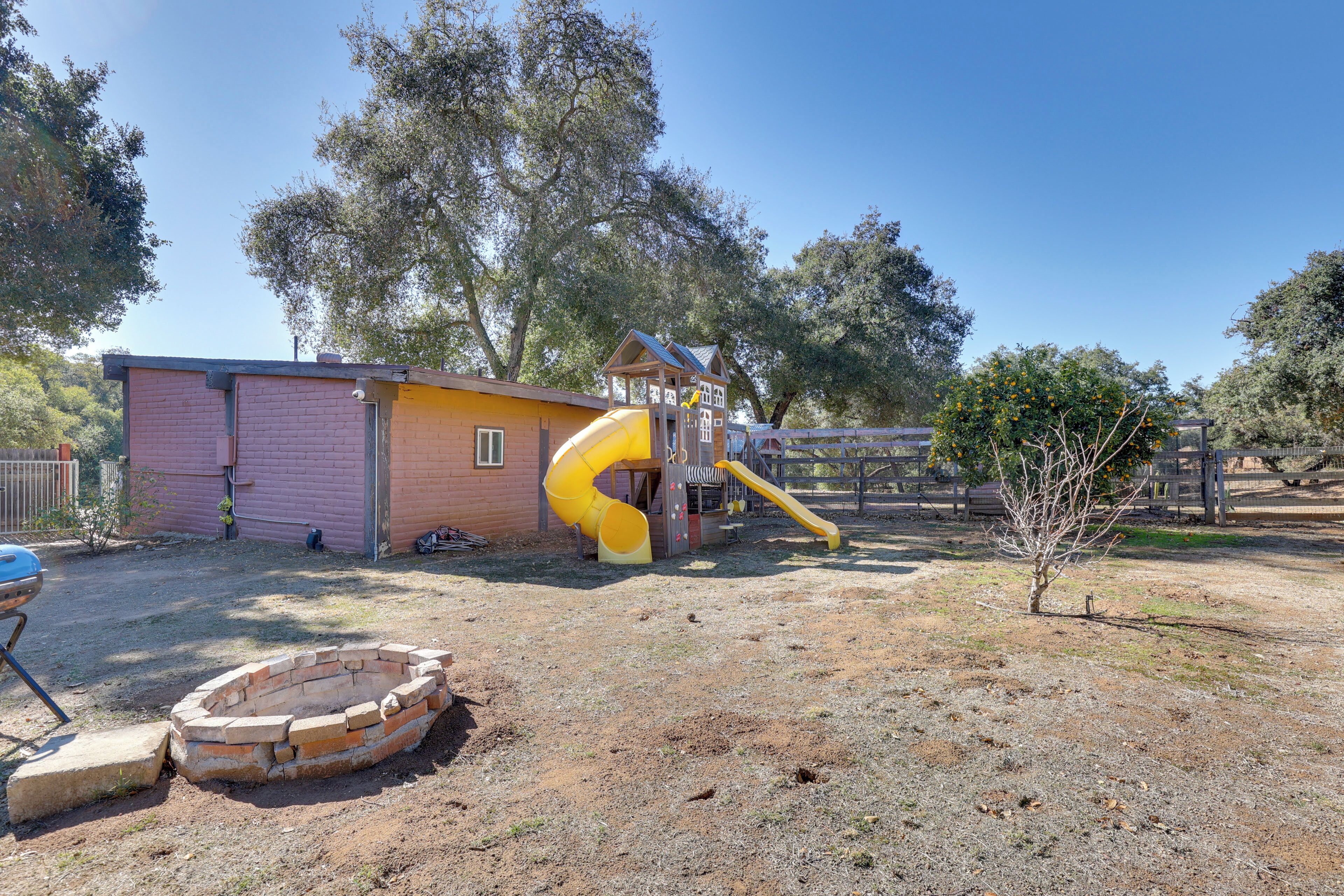 Ein Spielplatz mit Rutsche und Klettergerüsten, einer Spielhaus aus Ziegelsteinen und einem kleinen Baum.