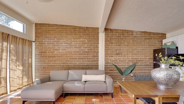 A living room with a brick wall, a sofa, a wooden table, and a large vase. - 5 Mi to Casino & Lake: Home on Escondido Ranch! (Escondido)