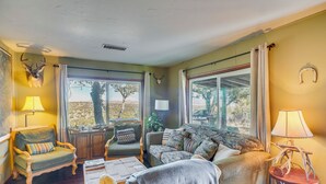 Un salon chaleureux avec une cheminée, des sièges confortables et de grandes fenêtres donnant sur l’extérieur.