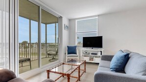 A living room with a sofa, a chair, a TV, and a glass table. - STEPS TO BONITA BEACH | SLEEP NUMBER KING BED | IN-UNIT WASHER/DRYER | BEACH GEAR INCLUDED (Bonita Springs)