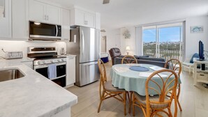 A modern kitchen with white cabinets, stainless steel appliances, and a dining area with a table and chairs. - STEPS TO BONITA BEACH | SLEEP NUMBER KING BED | IN-UNIT WASHER/DRYER | BEACH GEAR INCLUDED (Bonita Springs)