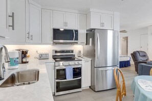 Una cocina moderna con armarios blancos, electrodomésticos de acero inoxidable, horno integrado y refrigerador.