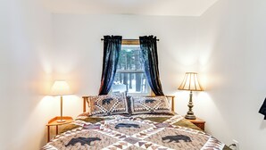 A bedroom with a bed, two bedside lamps, a window with curtains, and a view of trees outside. - 2 Ponds & Trail Access: Peaceful Cabin in Calumet! (Calumet)
