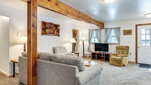 A living room with a grey sofa, a wooden chair, a television, and a wooden shelf. - 2 Ponds & Trail Access: Peaceful Cabin in Calumet! (Calumet)