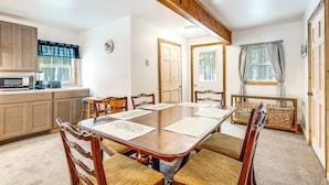 A dining room with a wooden table and chairs, a kitchen area with cabinets and appliances, and a view of the outdoors through a window. - 2 Ponds & Trail Access: Peaceful Cabin in Calumet! (Calumet)