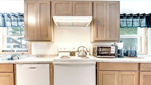 A kitchen with wooden cabinets, a white stove, a dishwasher, and a microwave. - 2 Ponds & Trail Access: Peaceful Cabin in Calumet! (Calumet)