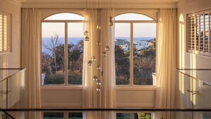 A room with a large arched window, a chandelier, and a view of houses and trees. - Mount Martha Manor Indoor Pool & Ocean Views (Mount Martha)