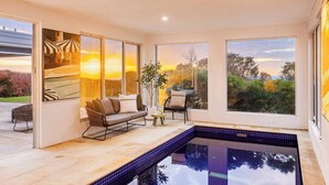 A modern indoor pool area with a view of a sunset landscape through large windows. - Mount Martha Manor Indoor Pool & Ocean Views (Mount Martha)