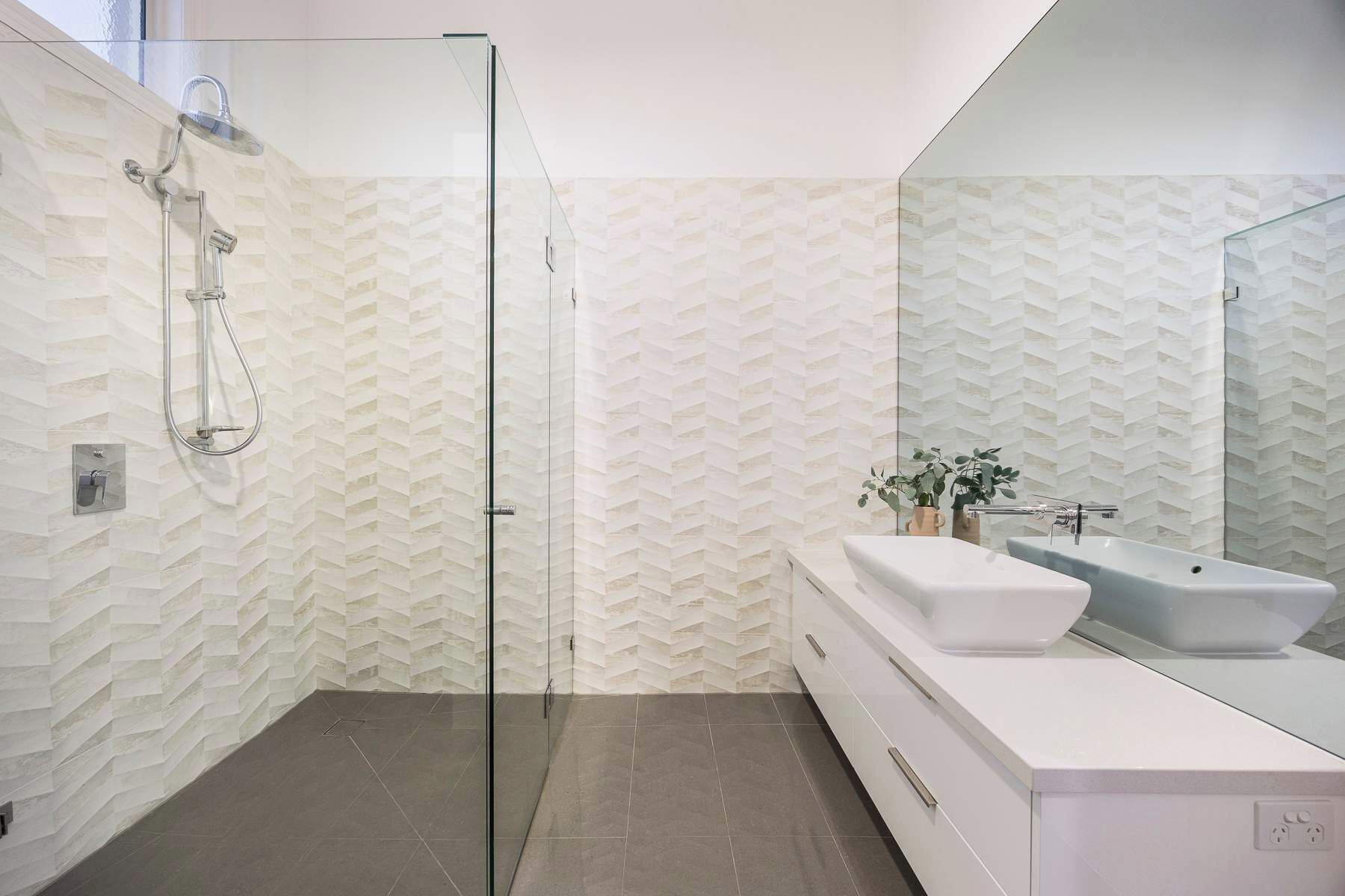 A modern bathroom with a glass shower enclosure, a white sink, and a large mirror.