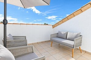 Un espace extérieur aménagé avec deux canapés en osier et une table, une pergola surmontée d’une toile blanche et un sol carrelé.