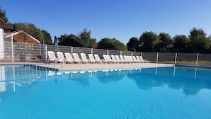 A swimming pool with white lounge chairs and a covered seating area. - Nice apartment for 2 guests with WIFI, pool, TV, terrace and pets allowed (De Haan)