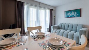A dining area with a table set for two, a sofa, and a painting on the wall. - Nice apartment for 2 guests with WIFI, pool, TV, terrace and pets allowed (De Haan)