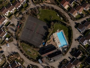 An aerial view of a residential area with a large rectangular building, a swimming pool, and a tennis court.