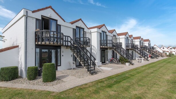 A row of modern, white buildings with red-tiled roofs, featuring balconies and external staircases. - Nice apartment for 2 guests with WIFI, pool, TV, terrace and pets allowed (De Haan)