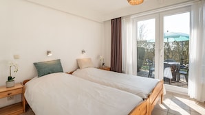 A bedroom with two beds, a large window, and a balcony with outdoor furniture. - Nice apartment for 2 guests with WIFI, pool, TV, terrace and pets allowed (De Haan)