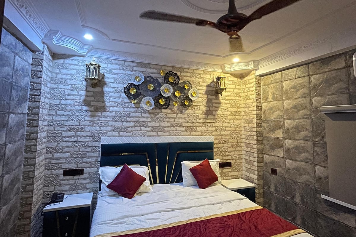 A bedroom with a stone wall, a bed with white bedding and red pillows, a ceiling fan, and decorative wall art.