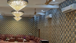 A room with a patterned wall, a chandelier, ceiling fans, and a seating area with a sofa and tables. - Sparrow Farms And Resort (Mohanlalganj)