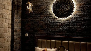 A bedroom with a stone wall, a decorative ceiling light, a bed with white bedding and red pillows, and a nightstand with a lamp. - Sparrow Farms And Resort (Mohanlalganj)