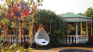 A hanging chair in a garden area with a gazebo in the background. - Sparrow Farms And Resort (Mohanlalganj)
