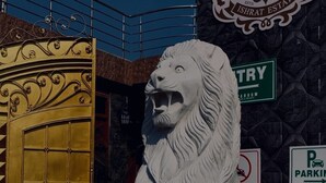 A lion statue in front of a building with a sign that reads "ISHRAT ESTATE". - Sparrow Farms And Resort (Mohanlalganj)