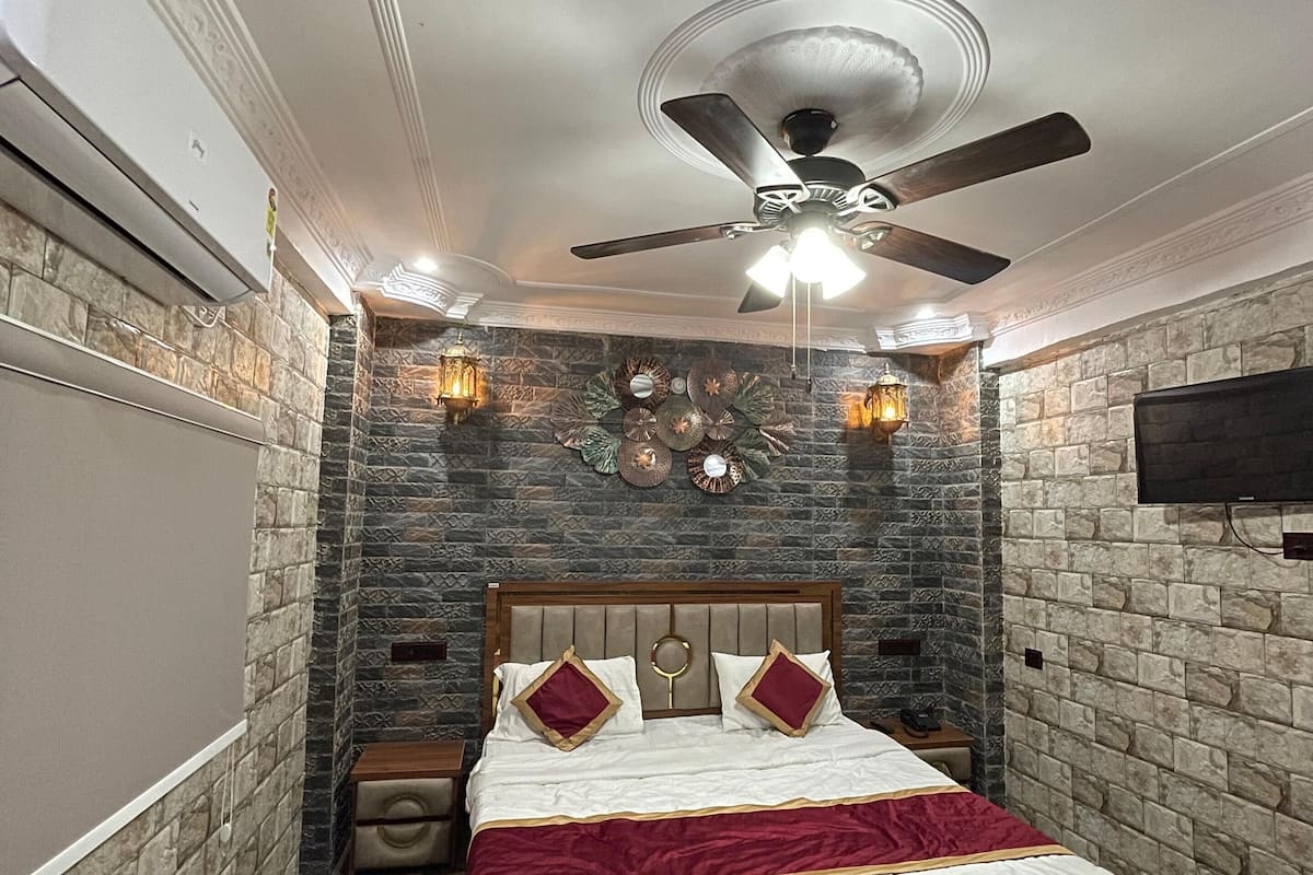 A bedroom with a stone-patterned wall, a wooden bed with a headboard, a ceiling fan, and a patterned rug.