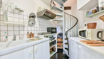 A compact kitchen with white cabinets, a microwave, a kettle, and a spiral staircase leading to a pantry.