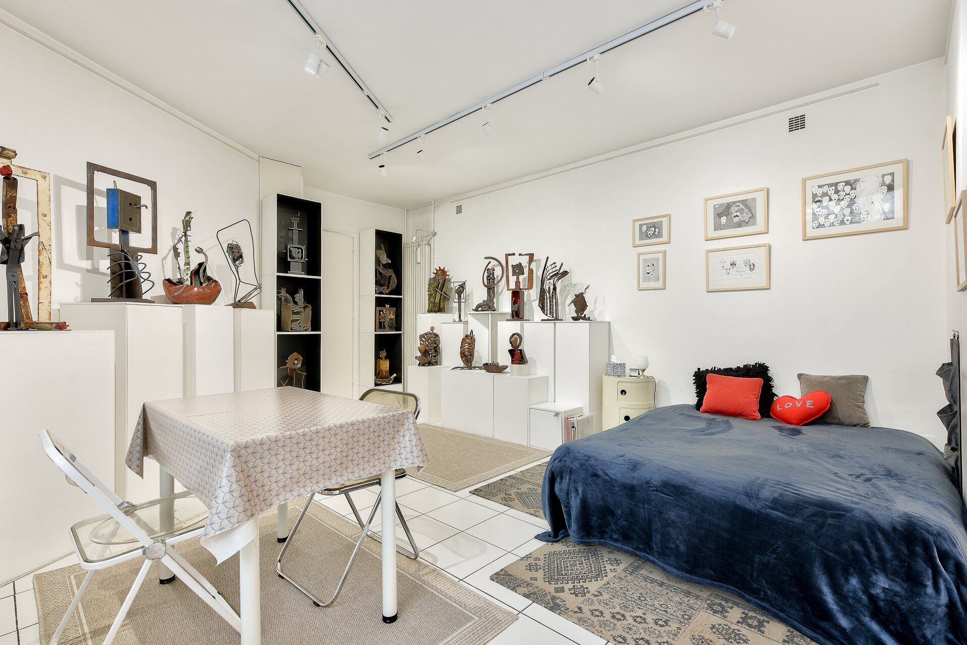 Quarto com cama, escrivaninha, estantes com objetos decorativos e quadros nas paredes.