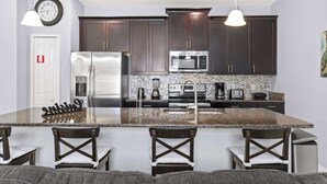 A modern kitchen with dark cabinets, stainless steel appliances, a granite island, and pendant lighting. - Spacious 4BR Townhome with Pool at Storey Lake (Kissimmee)