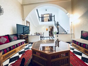 A spacious living room with a high ceiling, a central coffee table, a television, and a staircase leading to an upper level. - TYPICAL RIAD HOUSE MARRAKECH G7 - N51 (Marrakech)