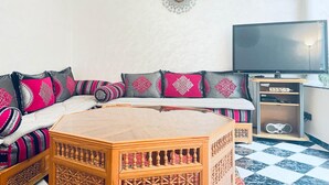 A living room with a sofa, patterned cushions, a wooden coffee table, a TV, and a shelf with electronic devices. - TYPICAL RIAD HOUSE MARRAKECH G7 - N51 (Marrakech)
