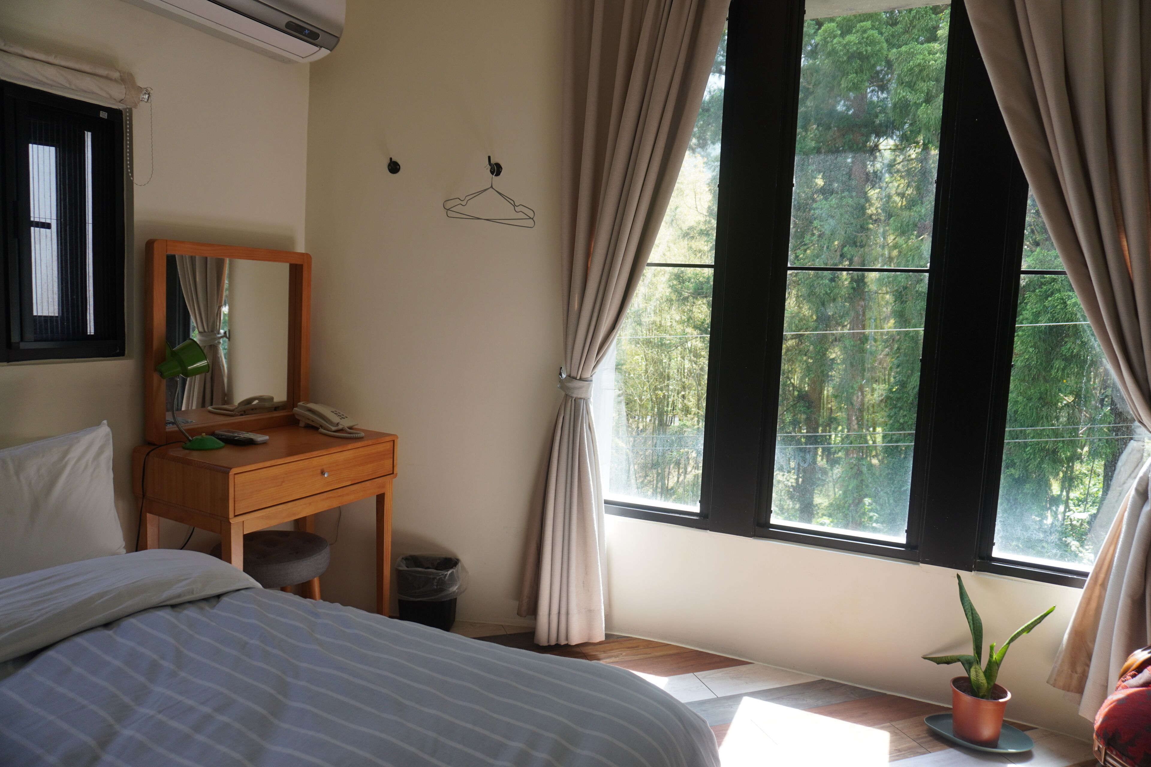 Un dormitorio con una cama, un escritorio de madera con un espejo, un teléfono y una planta en maceta.