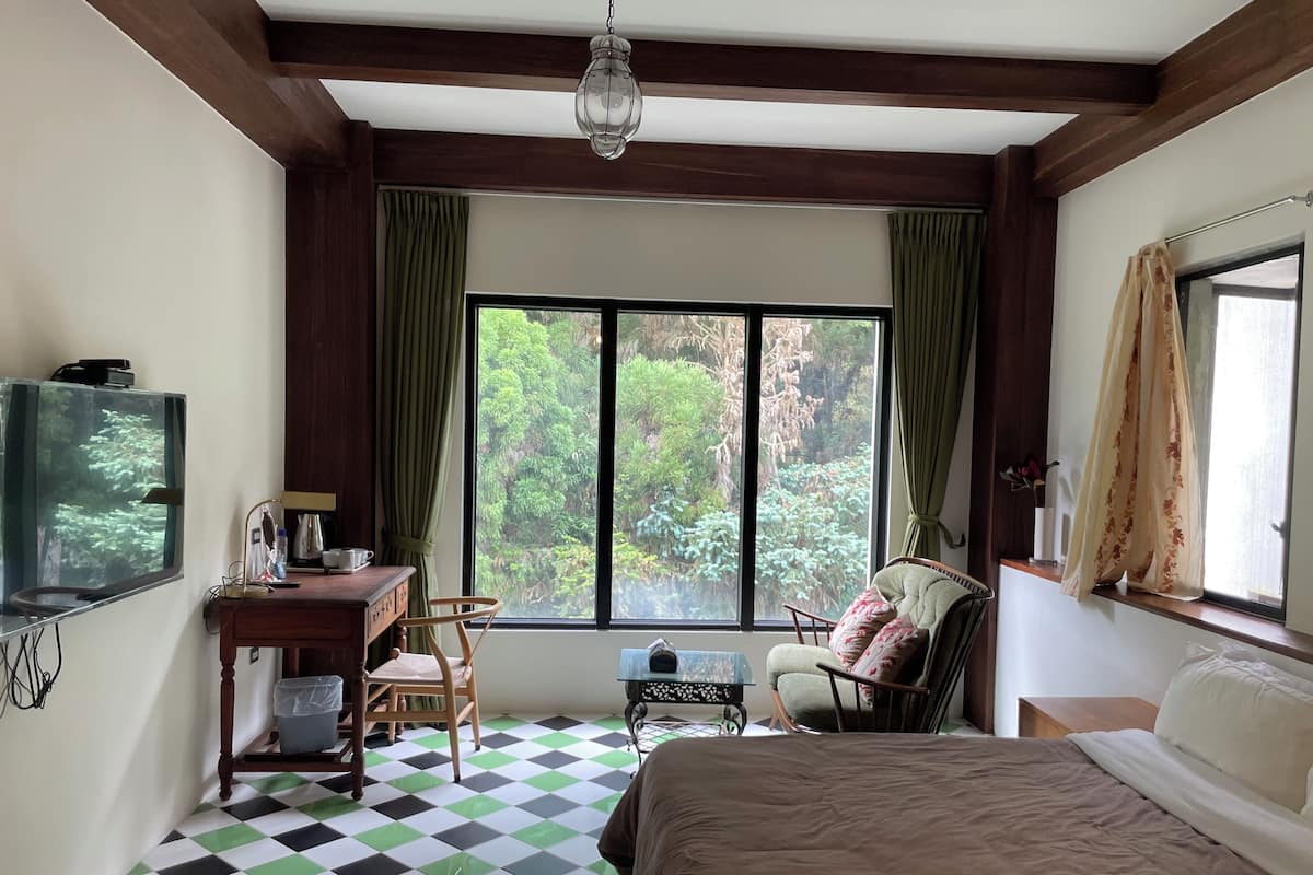 A room with a bed, a desk with a television, a chair, and a window with curtains.