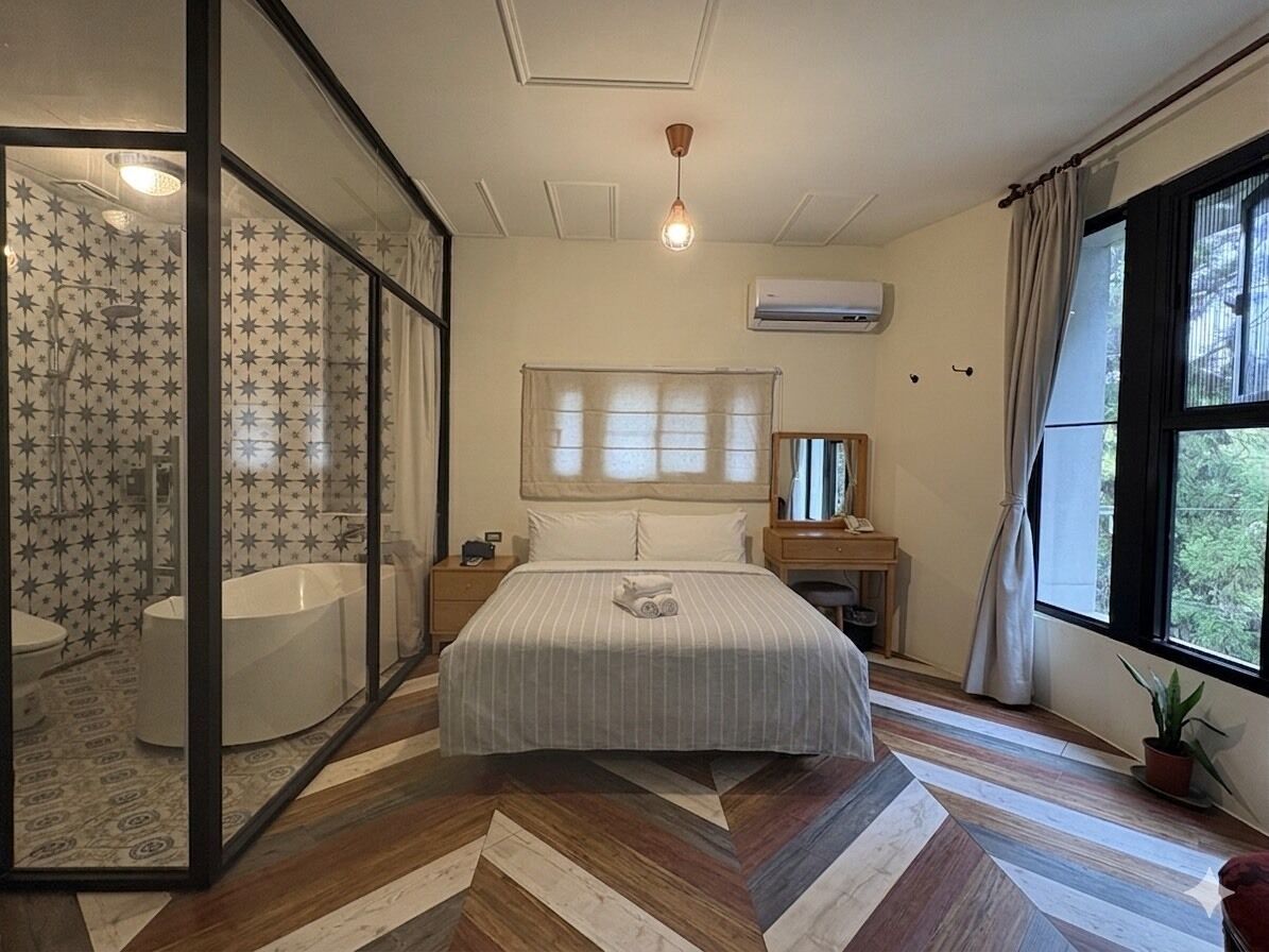 Un dormitorio con cama, mesita de noche, ventana con cortinas, equipo de aire acondicionado y vistas al exterior.