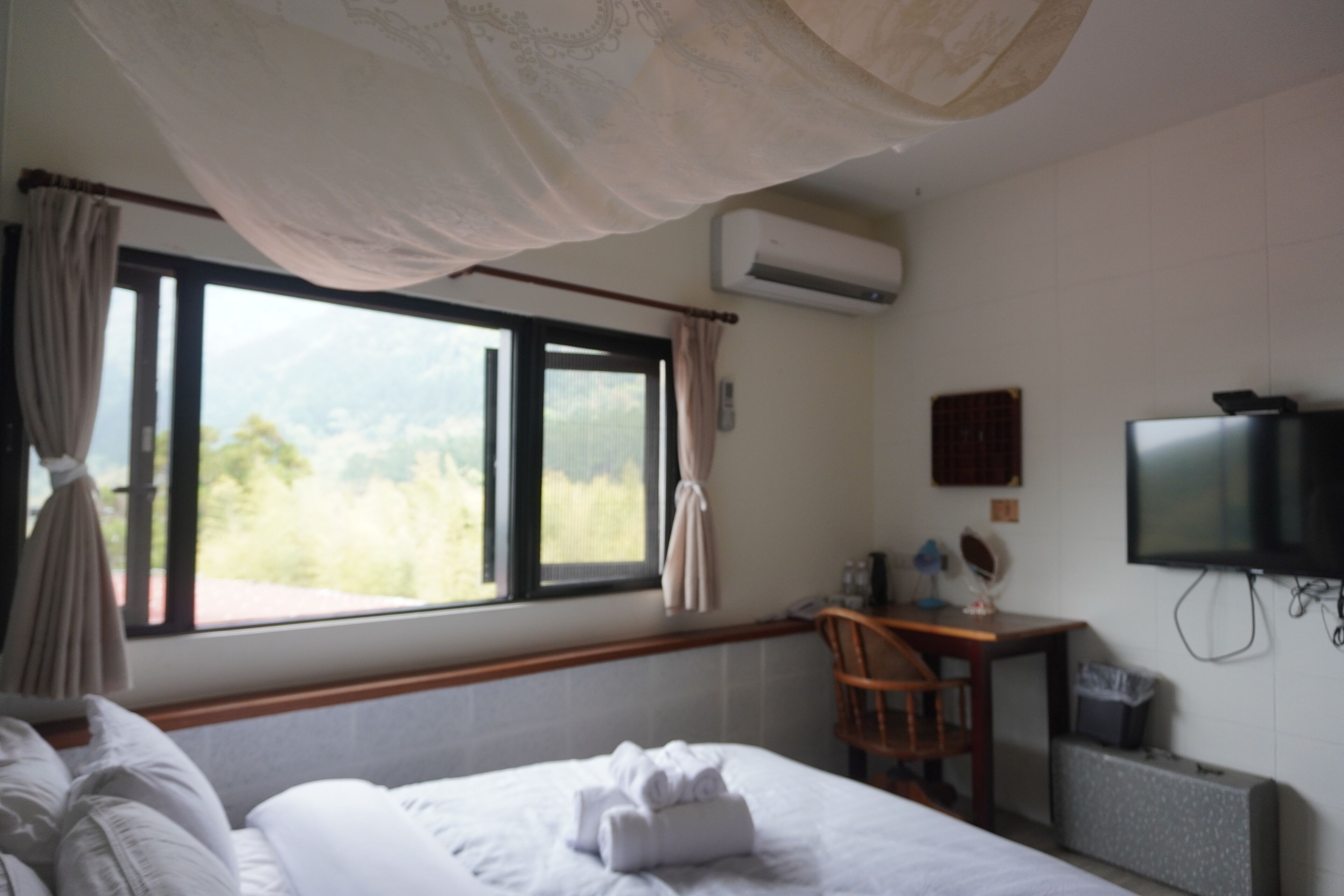 Una habitación de hotel con cama, escritorio, silla, televisión y aire acondicionado.