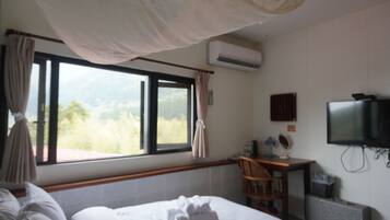 Una habitación de hotel con cama, escritorio, silla, televisión y aire acondicionado.