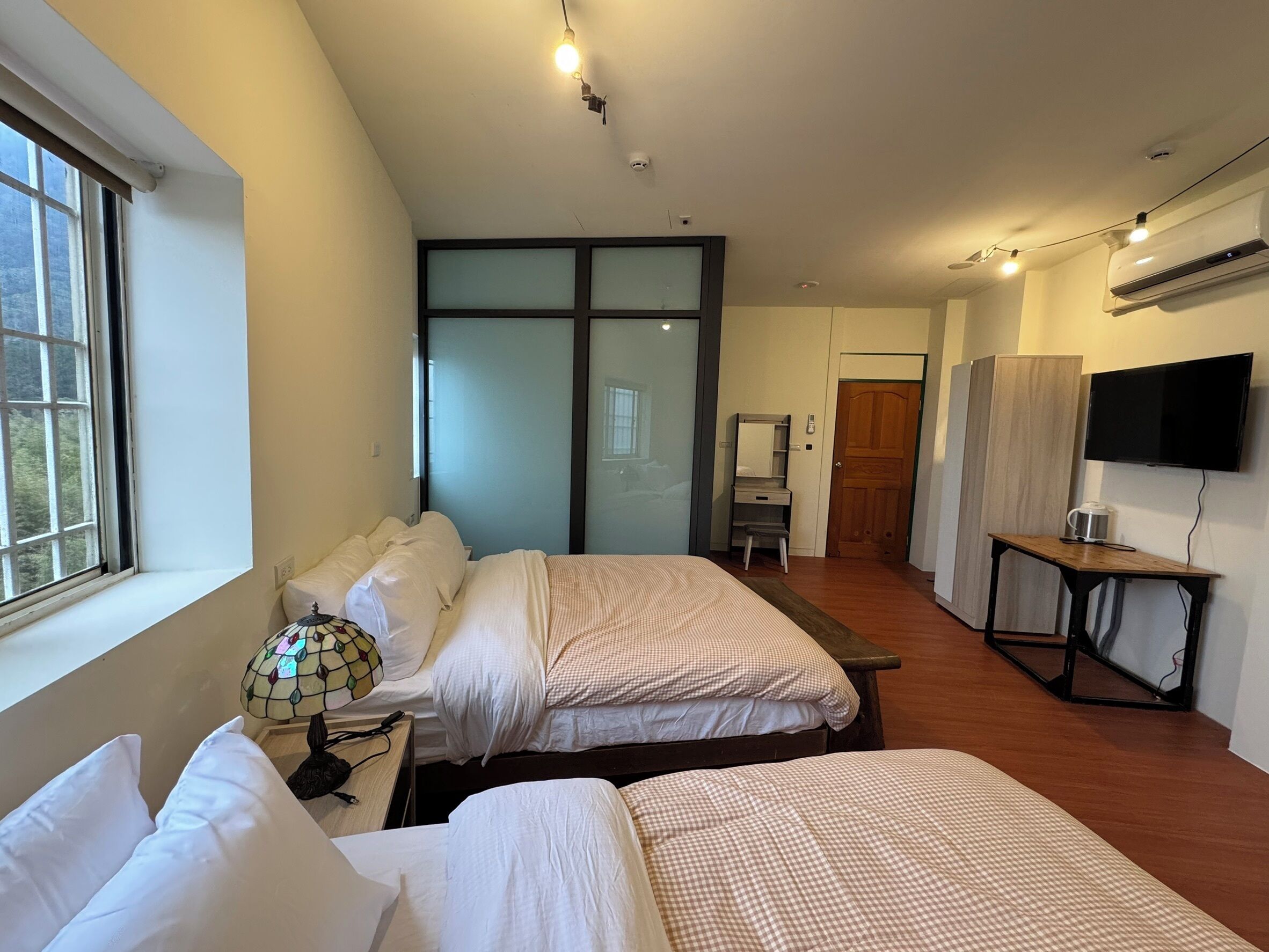 Un dormitorio con dos camas, un escritorio, un televisor y una ventana.