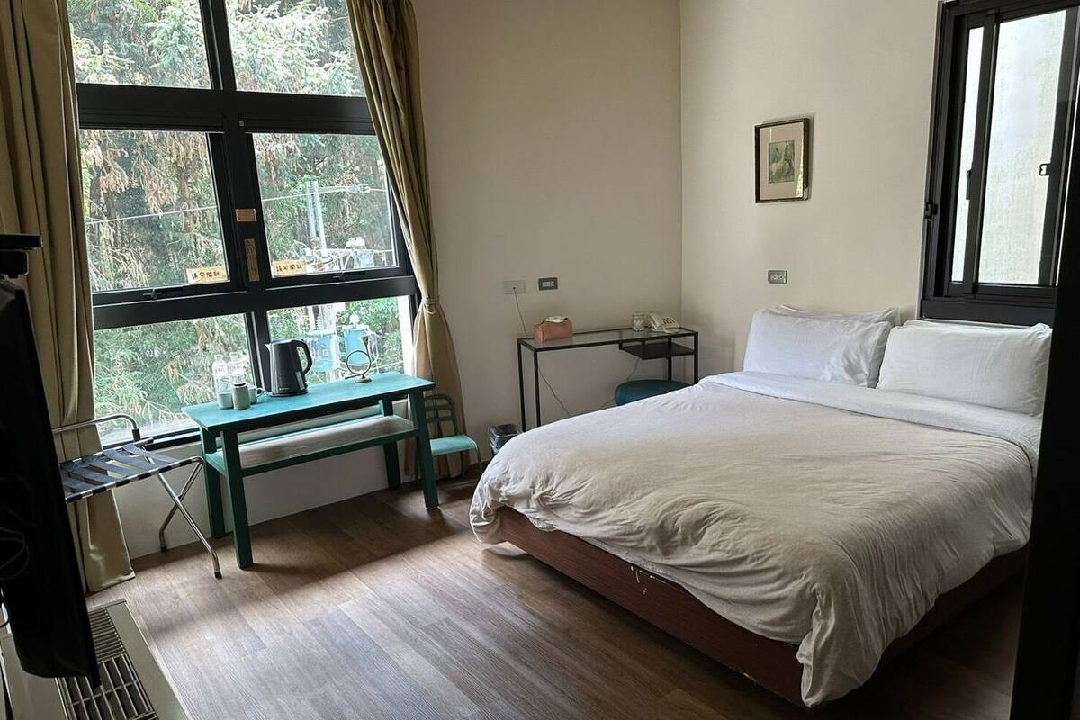 A bedroom with a bed, a desk, and a window with curtains.