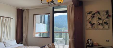 A hotel room with a bed, a sofa, a balcony with a table and chairs, and a desk with a refrigerator.