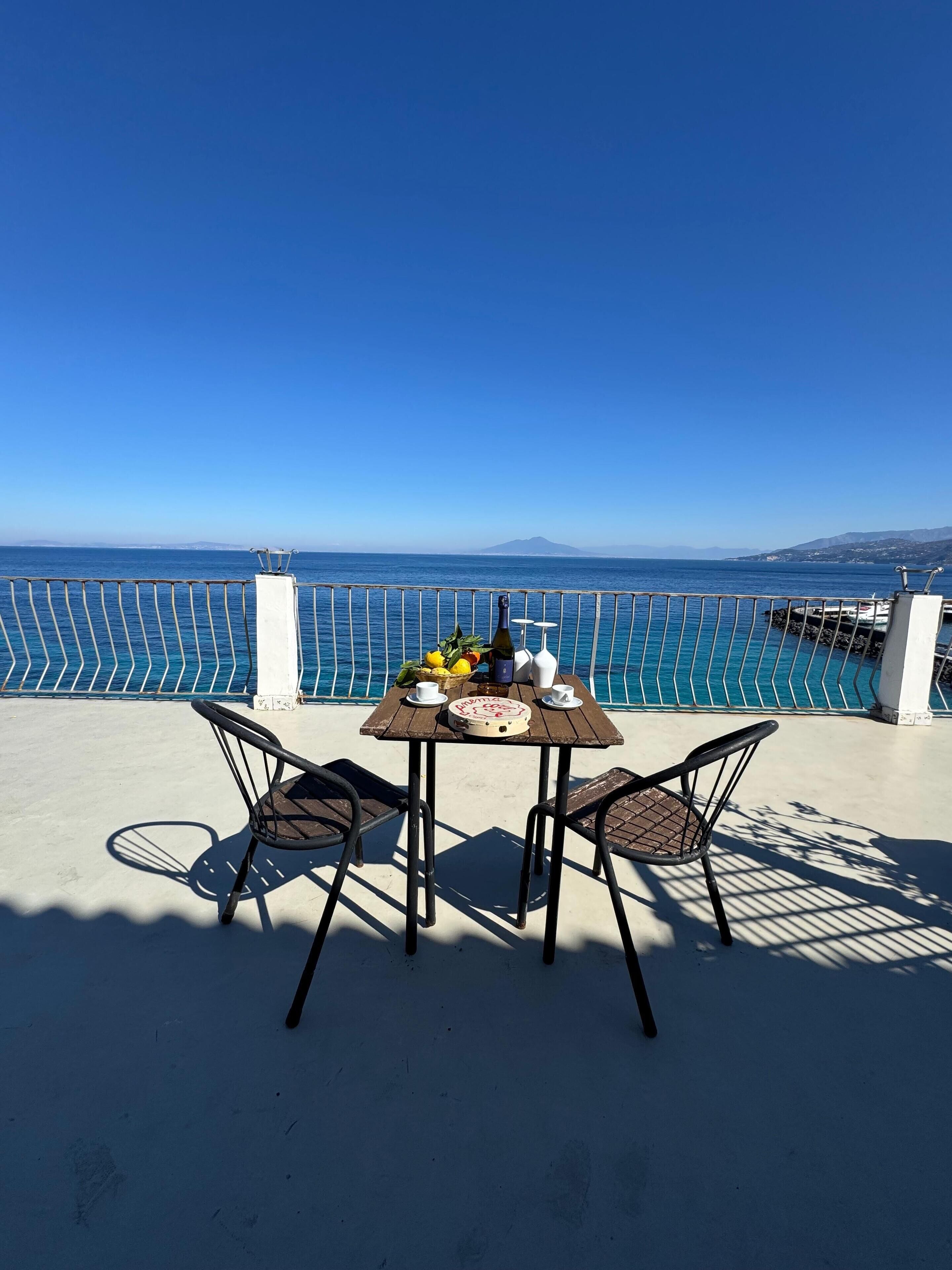 Una mesa con sillas en un balcón con vistas a una piscina y al mar.