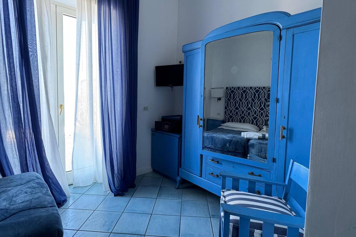 A room with a bed, a blue wardrobe, a television, and a window with curtains.