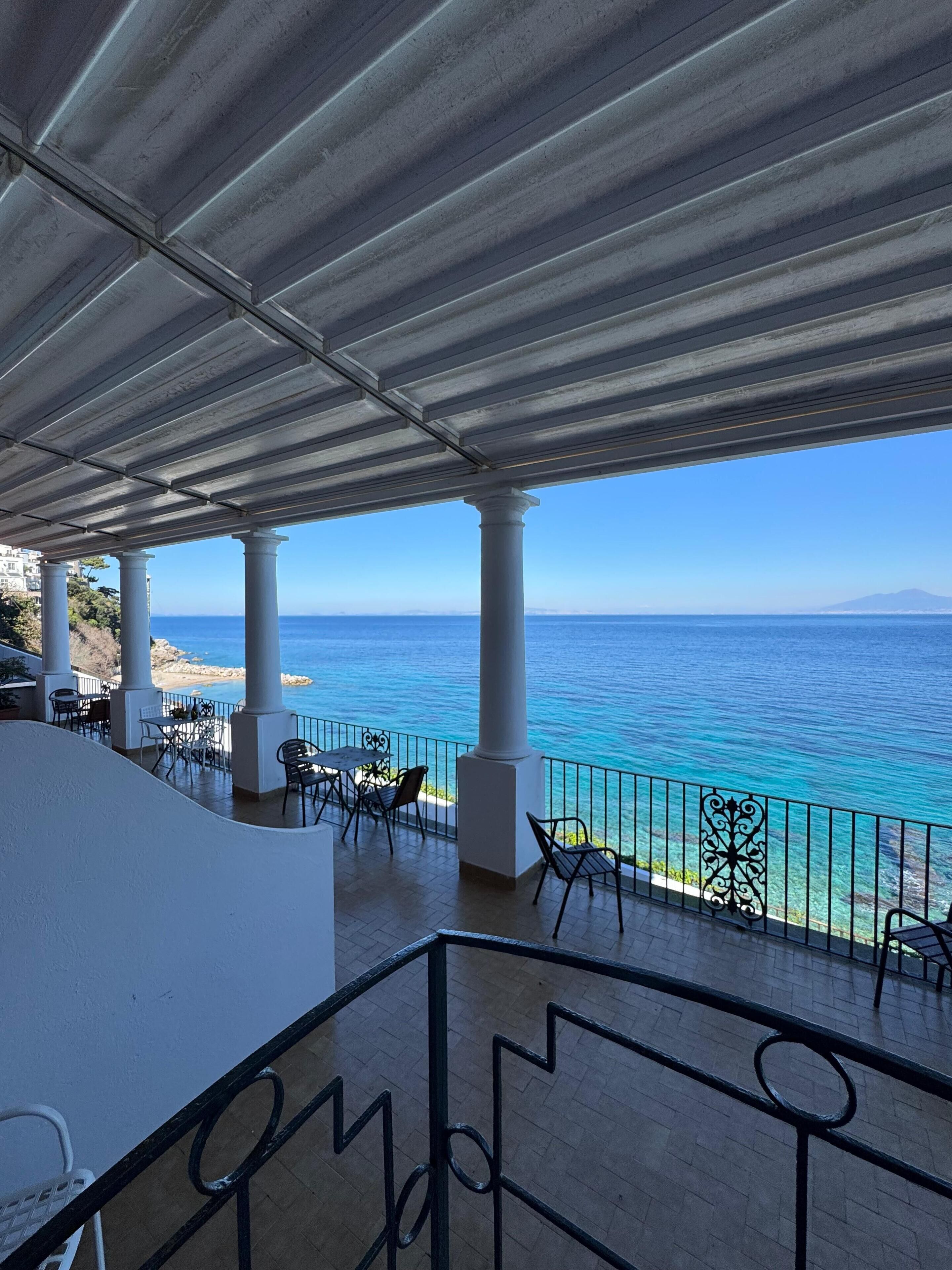 A terrace with a view of the sea, featuring outdoor seating and a railing.