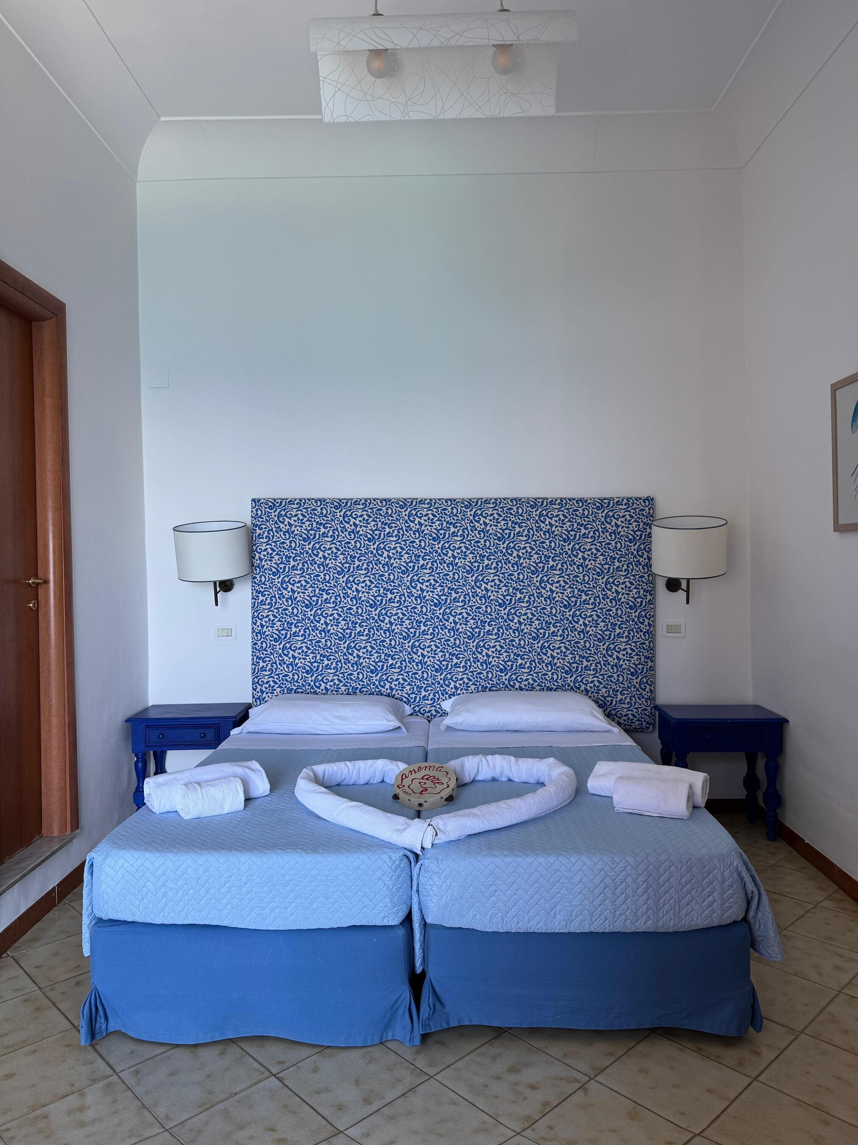 Una cama doble con un cabecero estampado en azul y blanco, dos mesitas de noche con lámparas, y una almohada decorativa sobre la cama.