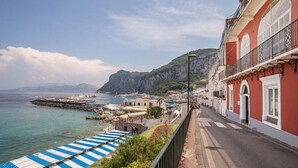 Un pueblo costero con un puerto deportivo, edificios con balcones y una vista despejada del mar y montañas al fondo.