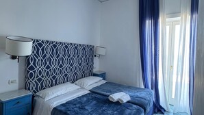 Un dormitorio con cama, mesita de noche, lámpara y ventana con cortinas.