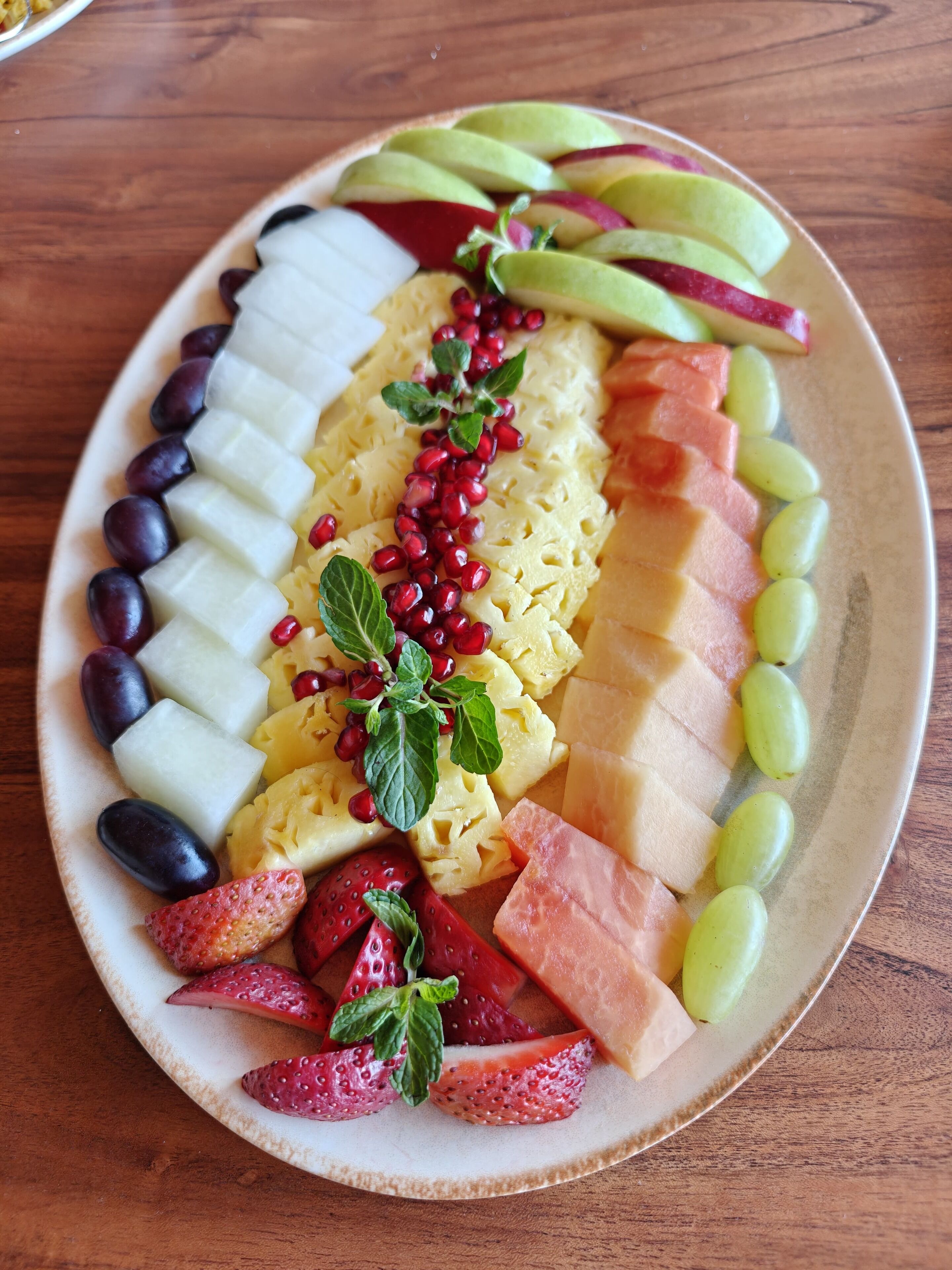 A plate of assorted fruits including strawberries, grapes, pomegranate seeds, and melon slices.