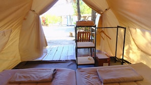A tent with two beds, a wooden table, and a chair outside.