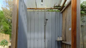 A small, enclosed outdoor shower area with a metal roof and wooden frame, featuring a showerhead and a handwashing station.
